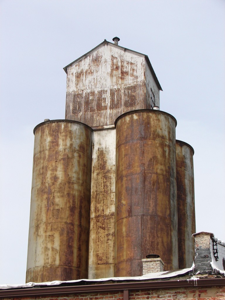 Four rusty grain elevators with house-shaped structure on top