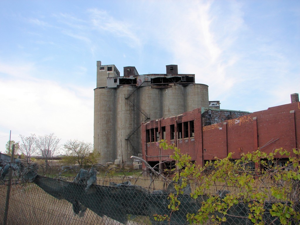 Chicago grain elevator with dilapidated brick building attached, viewed from behind barbed wire fence