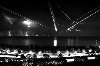 A beautiful lightning and plane long exposure panoramic compilation photograph along Lake Shore Drive and the lakefront of Lake Michigan in Chicago with water reflections and light trails.