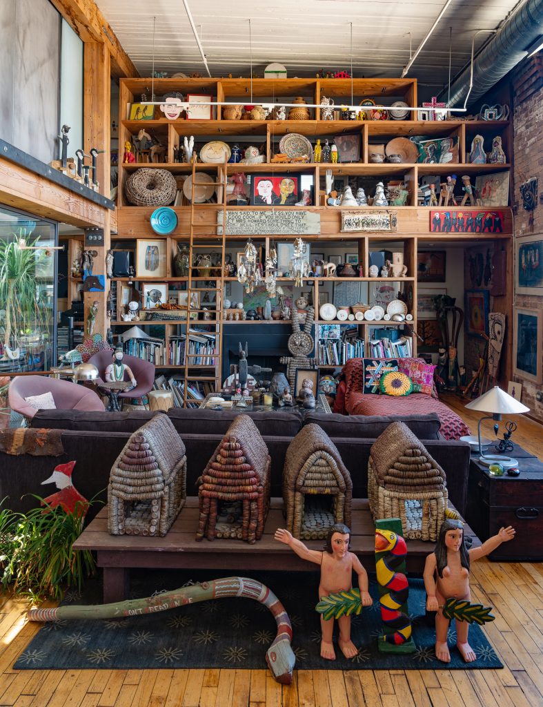 Photo of high-ceiling living room with art and books covering shelves and floor.