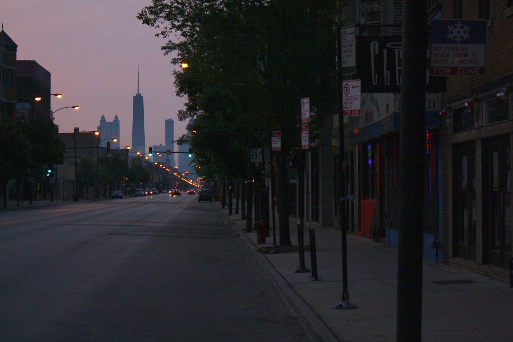Photograph of early morning view down a Chicago street with downtown skyscrapers including the Hancock in view in the distance.