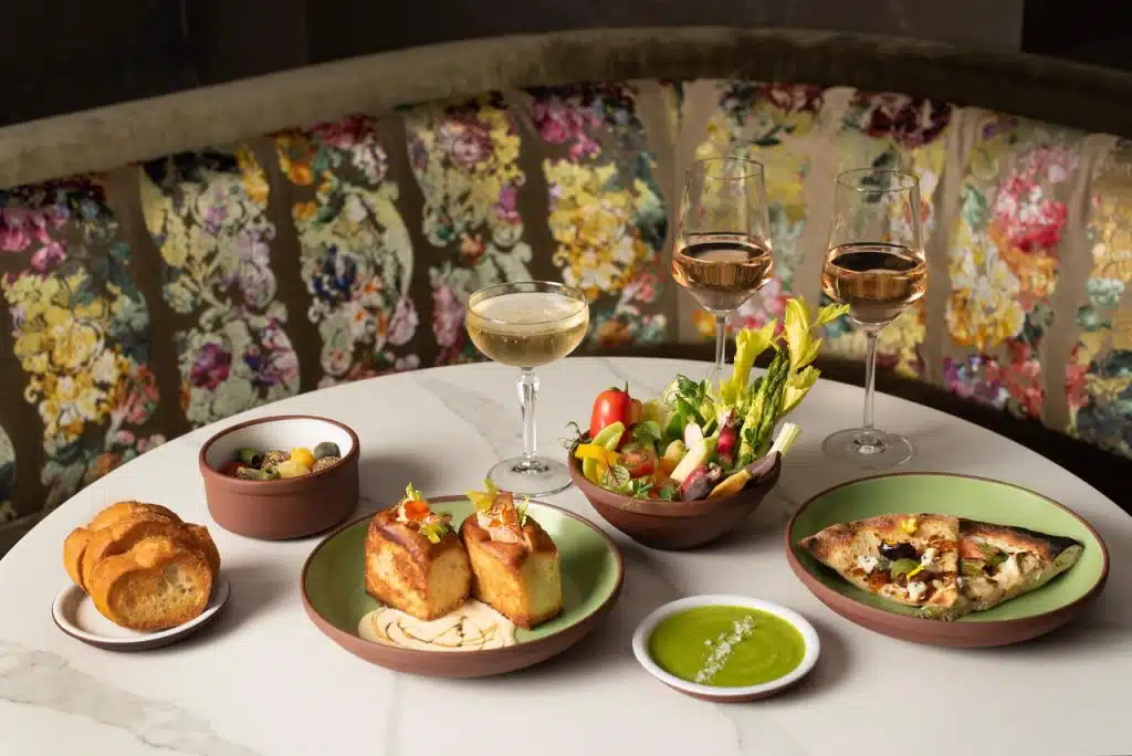 Photoraph of elegant round table with spread of appetizers and three wine glasses, with an ornate flower pattern booth behind it.