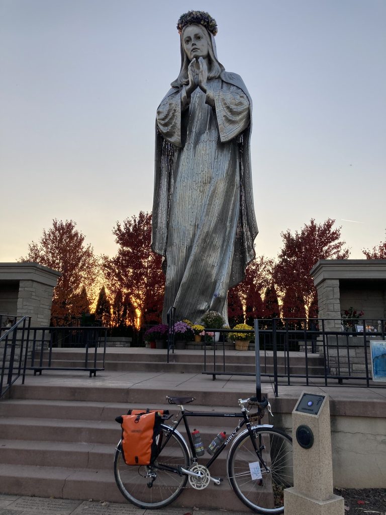Large silver statue of Mother Mary with sunset behind