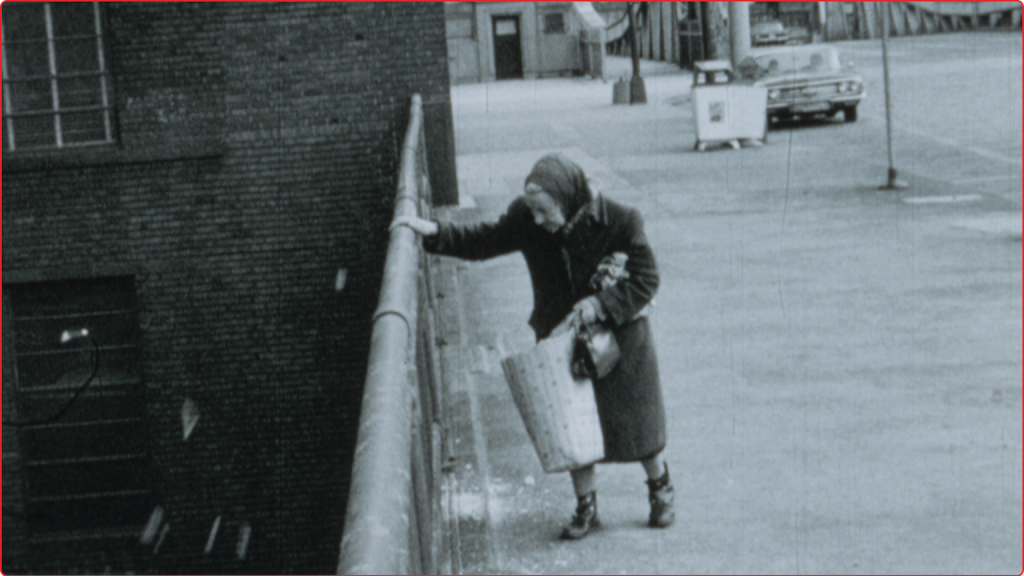 Woman in winter clothes hangs on to the top of a fence while holding a large bag.