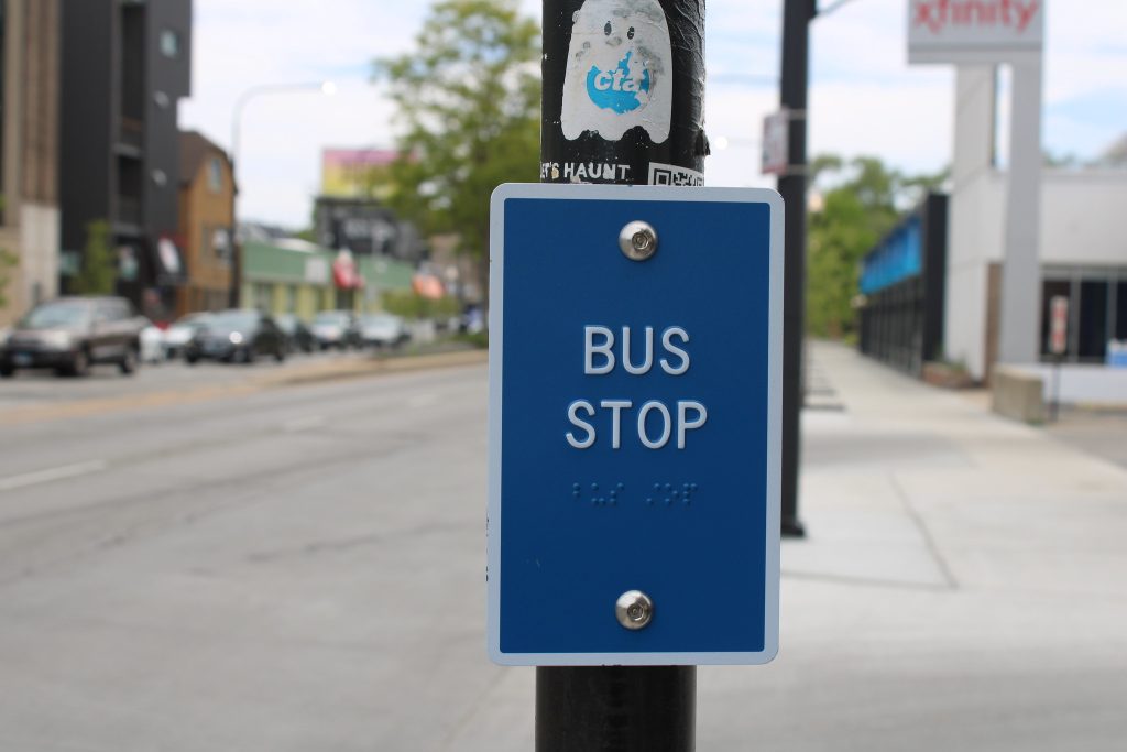 Photo of blue sign on pole that reads 'Bus Stop' in white letters