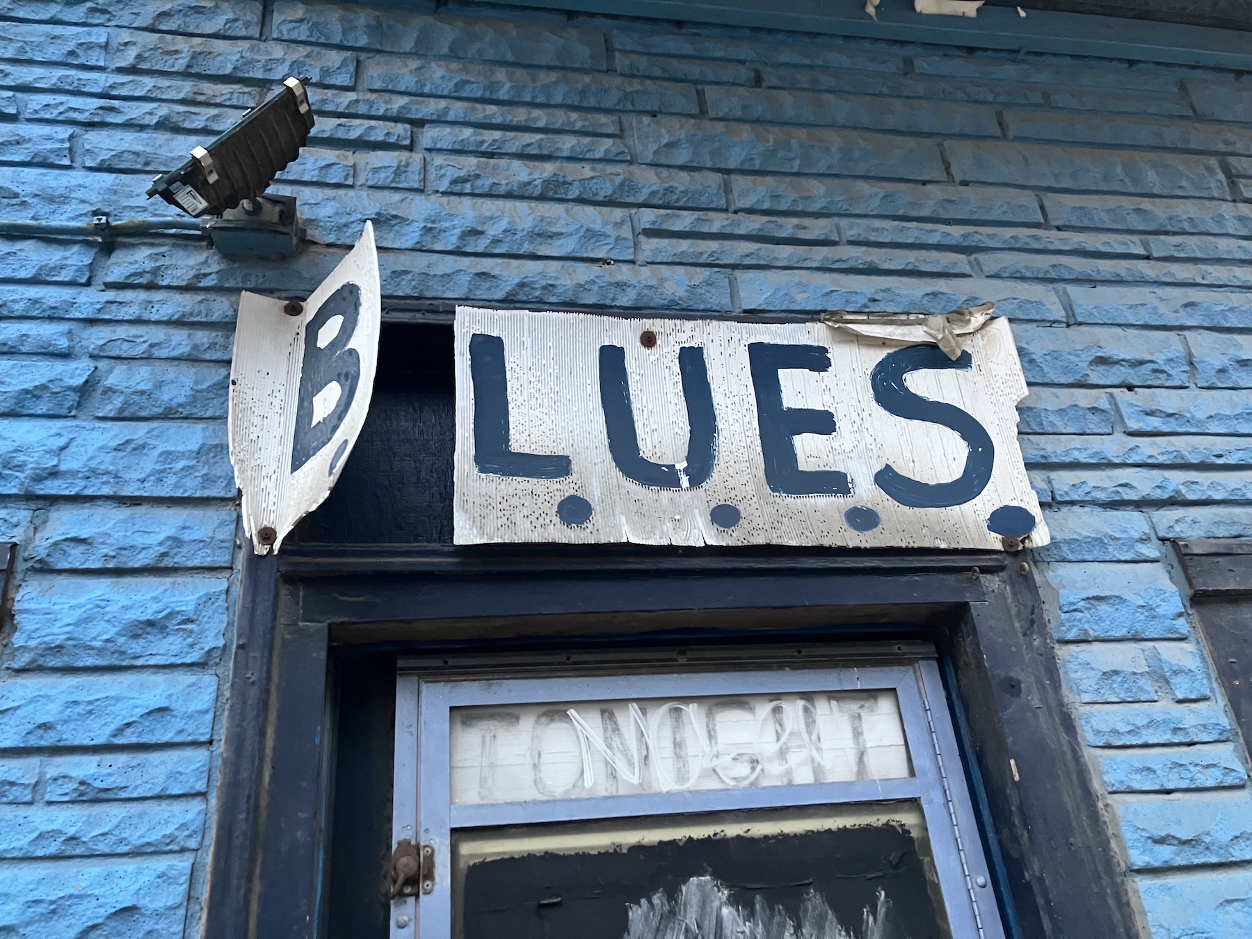 Sign that reads "B.L.U.E.S." over window opening on side of brick building.
